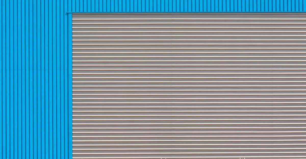 Façade d'un bâtiment industriel bleu avec porte roulant, mettant en avant l'architecture moderne.