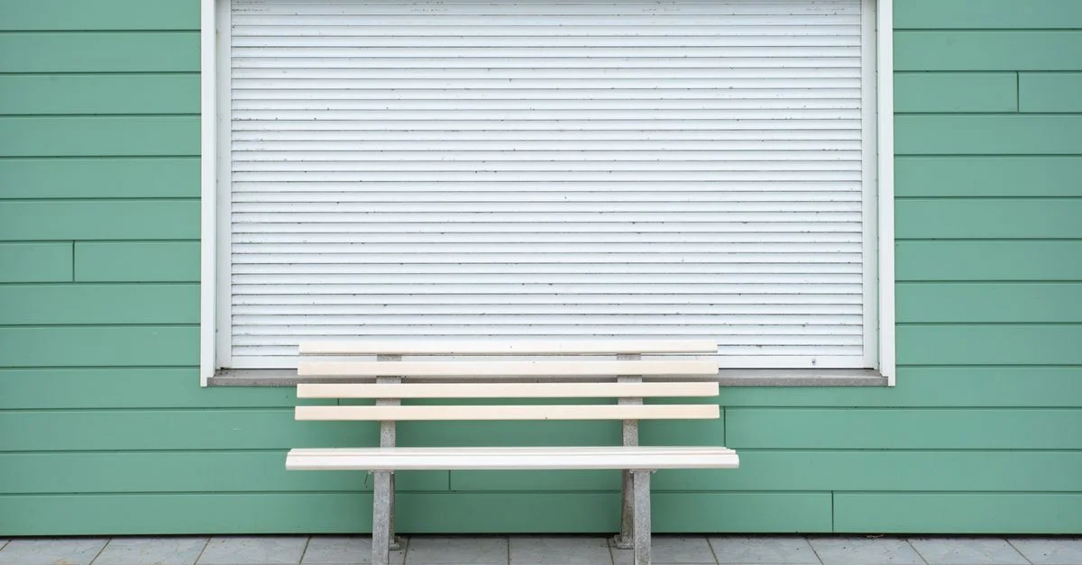 Simple banc en bois près d'un mur vert avec un rideau roulant fermé. Idéal pour une décoration minimaliste.