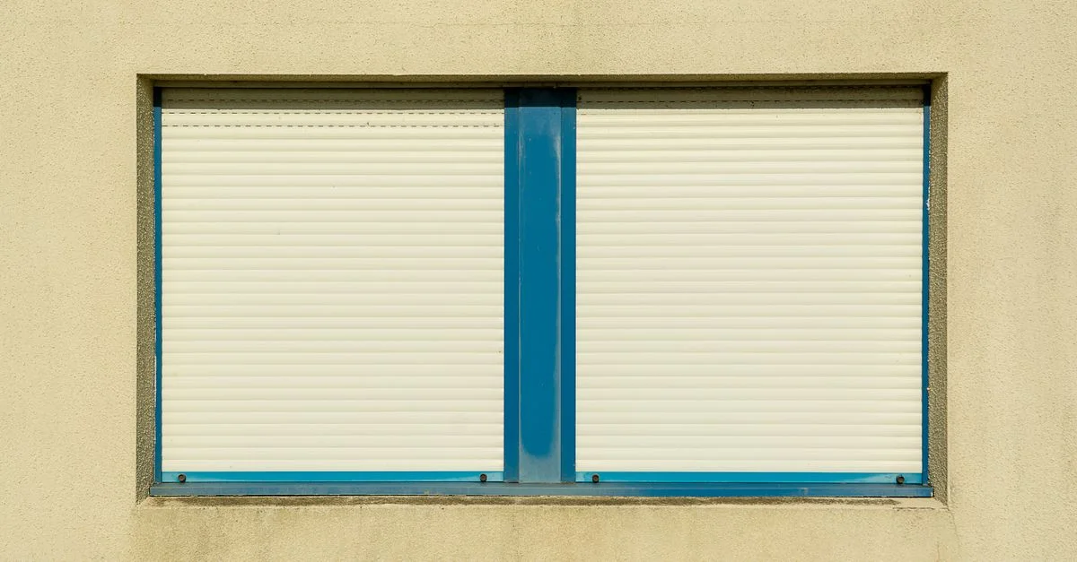 Gros plan d'un mur beige avec des volets fermés à cadre bleu, symbolisant la sécurité et l'intimité.