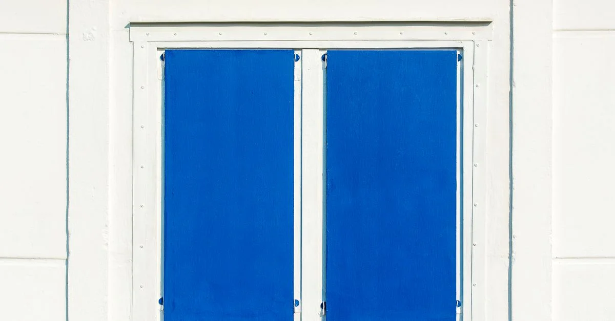 Gros plan sur un mur blanc avec une fenêtre à volets bleus, architecture minimaliste.