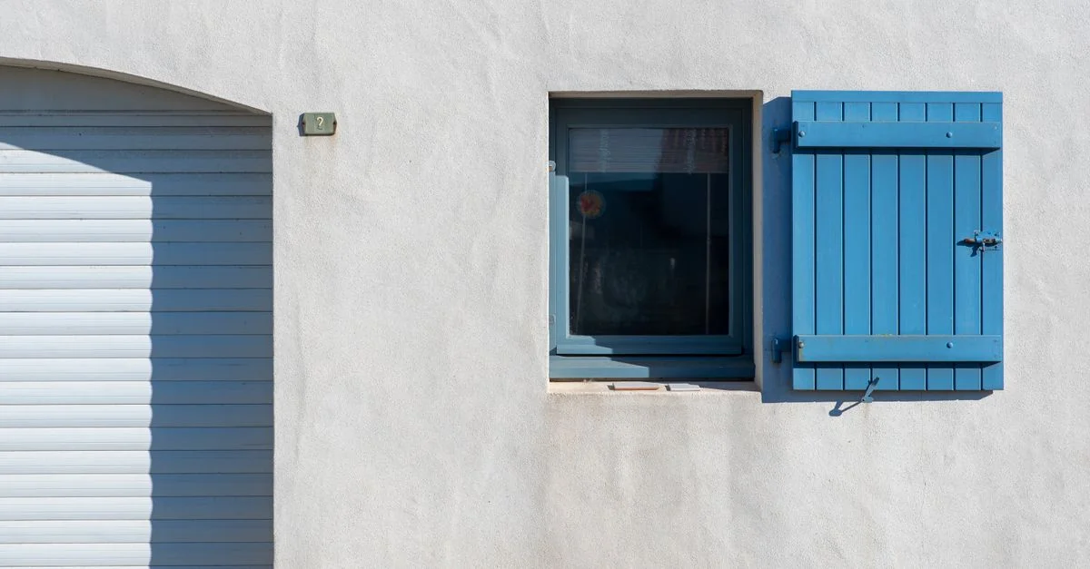 Façade minimaliste lumineuse avec volets bleus et mur blanc texturé.