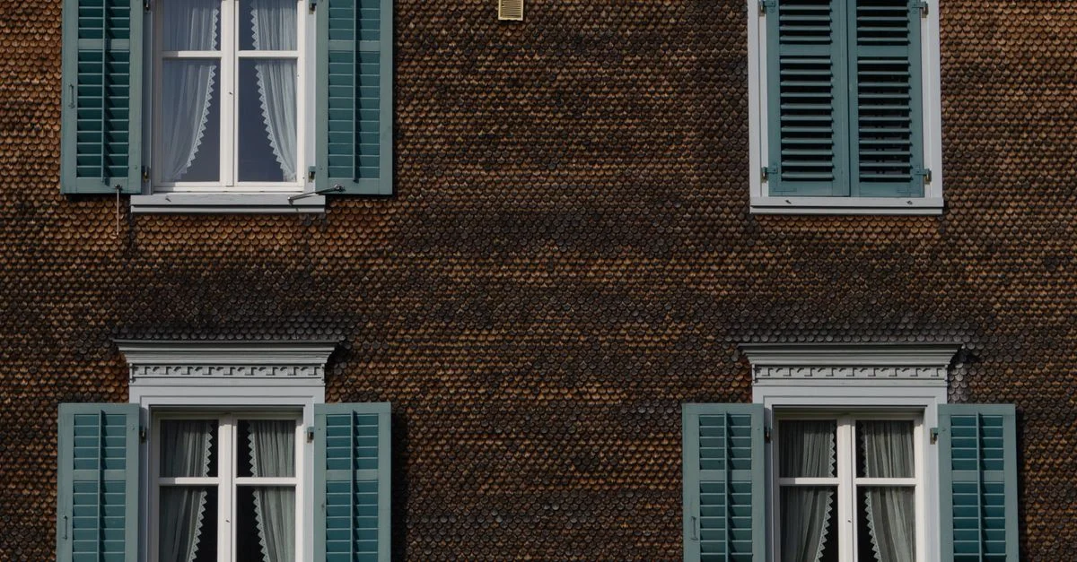Gros plan sur l'extérieur d'un bâtiment brun avec des volets de fenêtre verts et des rideaux.