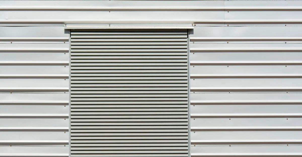 Gros plan d'une porte roulante en métal minimaliste sur un mur en tôle blanche, idéale pour des thèmes industriels.
